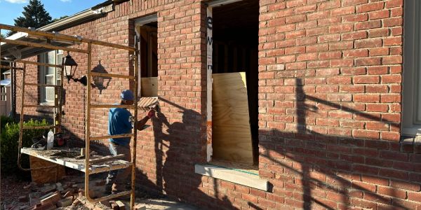 A construction worker measuring a window frame on a brick wall under sunlight.