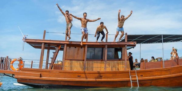 Four men jumping off a wooden boat into the water, enjoying a sunny day.