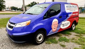 A parked van with a blue and red wrap. The back panel of the van has the McCoy Tygart logo. 