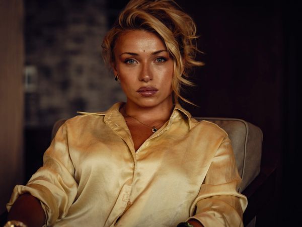 Woman in a satin beige blouse looking seriously at the camera.