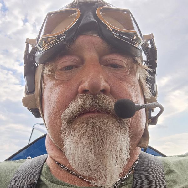 Close-up of a man wearing vintage pilot goggles and headset with a microphone.