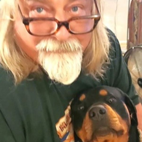 Man with glasses and beard holding a Rottweiler dog.