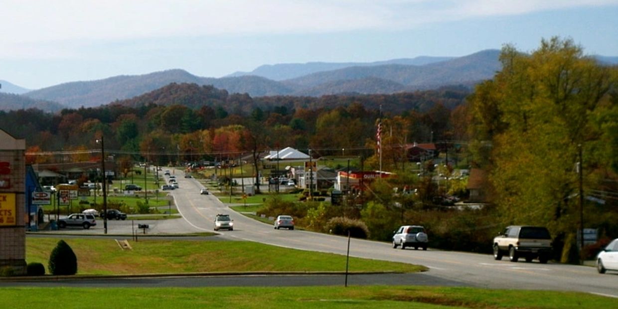 Small town road with cars and mountains in the background.