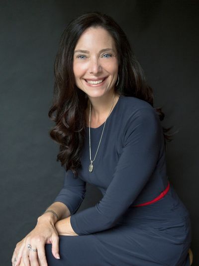 Woman in navy dress smiling with dark background.