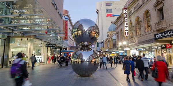 Two large reflective spheres stacked in a busy city street with people walking around.