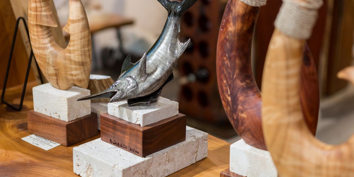 David Wirth marlin sculpture displayed among carved wood sculptures on fossil coral and wood bases.

