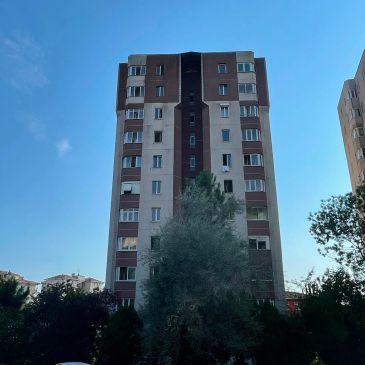 Gökyüzü altında 10 katlı apartman ve ağaçlar.