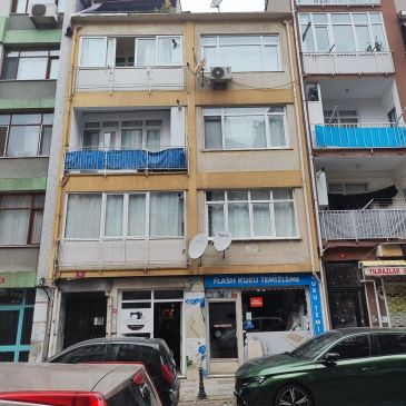 Dört katlı apartman ve önünde park etmiş arabalar.