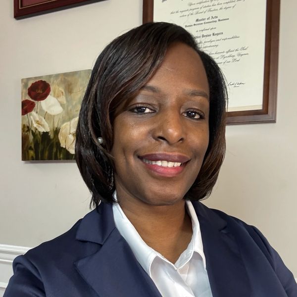 Woman smiling in business attire with framed pictures behind.