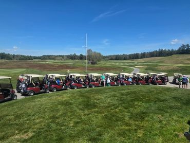 A line of golf carts parked on a sunny golf course with players nearby.
