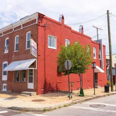 Red brick building on a street corner with signs and a tree.