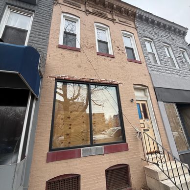 Boarded-up brick row house with stairs and metal railing.