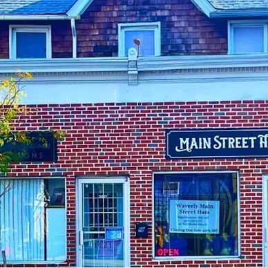 A brick storefront of Main Street Hats with a sale sign and open door.