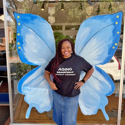 Smiling woman posing with blue butterfly wings painted on a window.