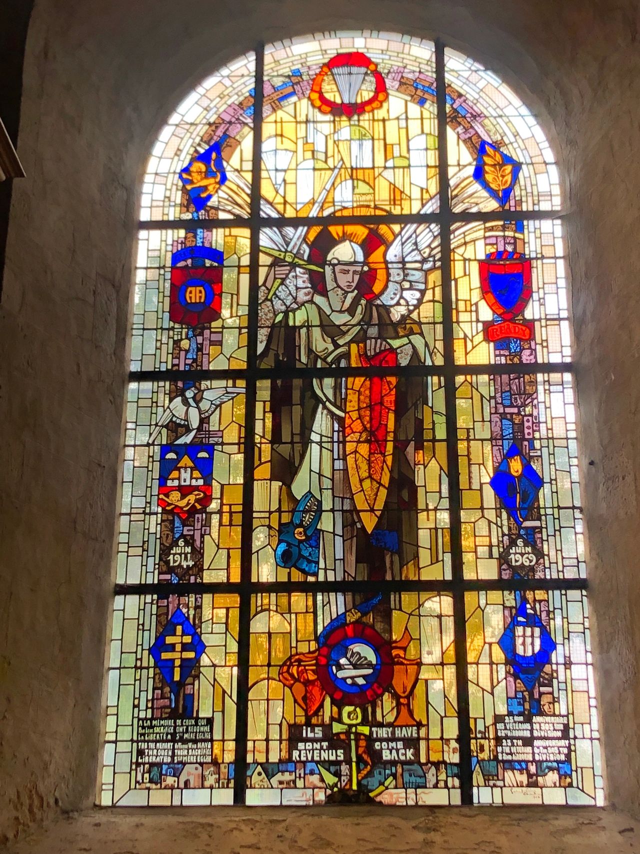 Sainte Mere Eglise: This stained glass window was installed in 1969, as American paratroopers returned to mark the 25th anniversary of D-Day. Note the words on the bottom in French and in English: they have returned. 