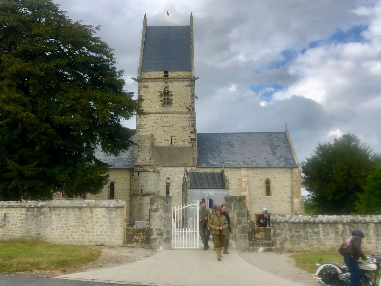 The small village church in Angoville au Plain with American GI re-enactors exiting the grounds around the 75th anniversary of D-Day. 