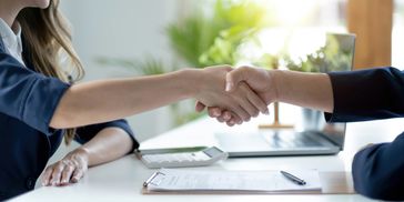Two people shaking hands over a white table