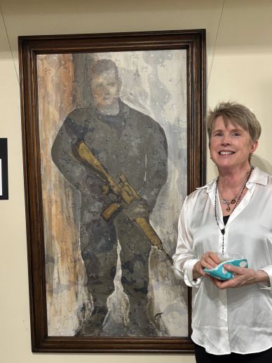 Woman standing next to a framed painting of a person with a rifle.