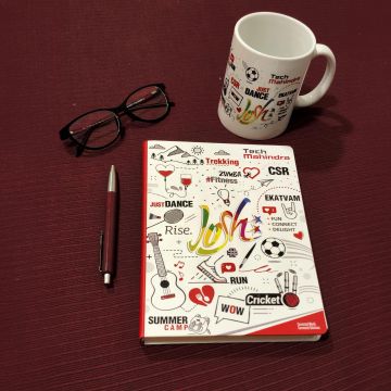 Notebook, glasses, pen, and a mug on a red surface.