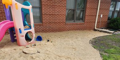 Children's playground slide set in a sandpit near a brick building.