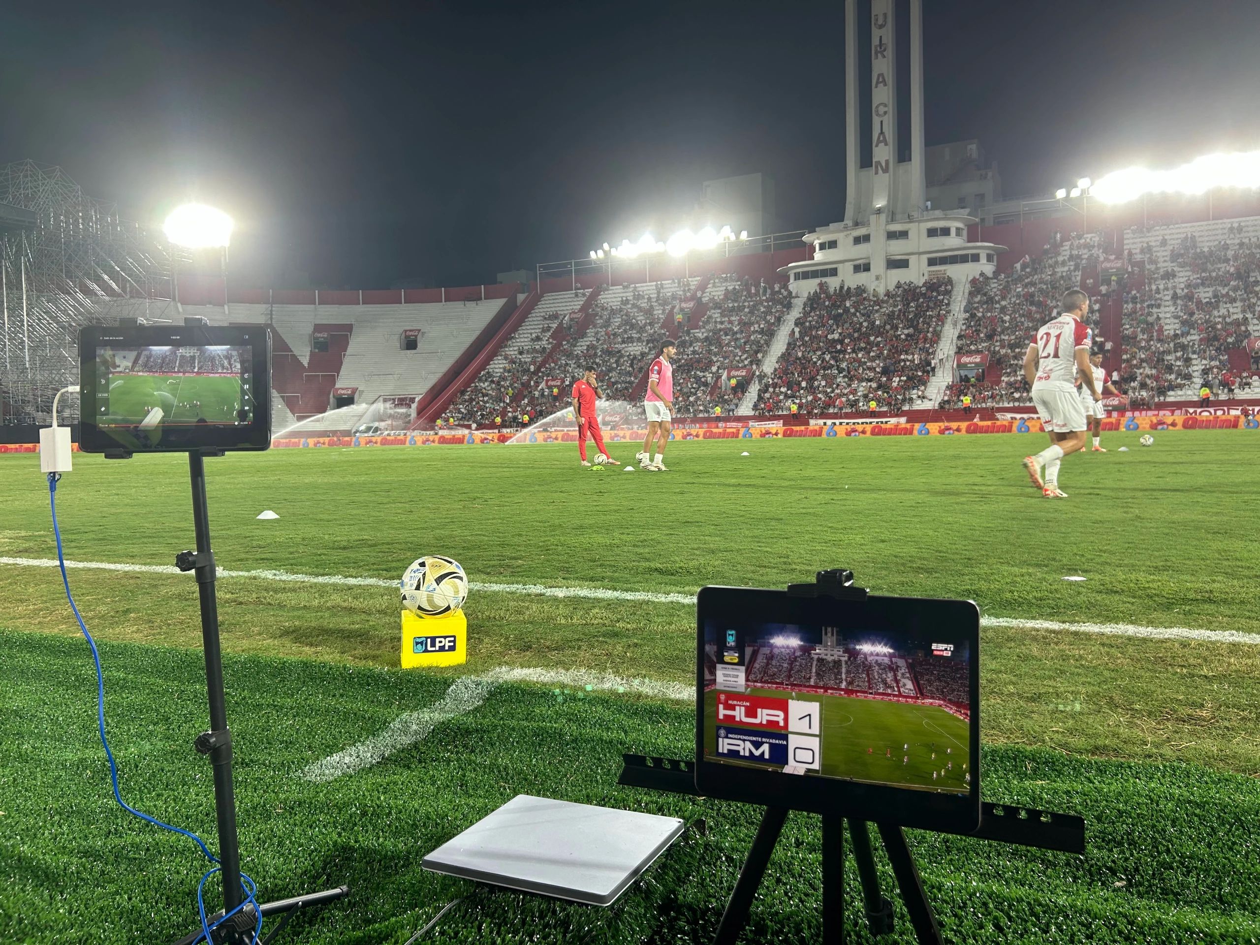 Campo de fútbol con jugadores calentando y espectadores en las gradas.