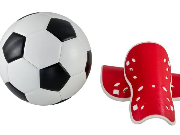 A classic black and white soccer ball next to a pair of red shin guards.