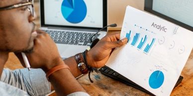Man analyzing data charts on paper and laptop.