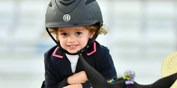 A young child smiling while riding a horse, wearing a helmet and jacket.