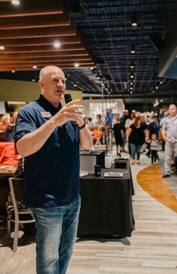 Man speaking into microphone at a crowded indoor event.