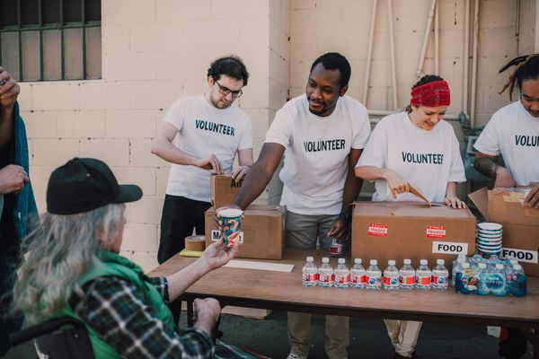 Volunteers distributing food and water to a person in need outdoors.