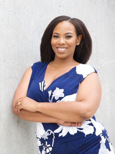 Confident woman smiling with arms crossed in blue floral dress.