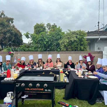 A group of people wearing chef hats having a backyard barbecue.