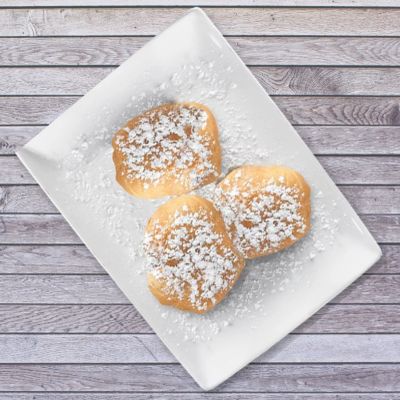 Three powdered sugar-covered Beignets on a white plate.