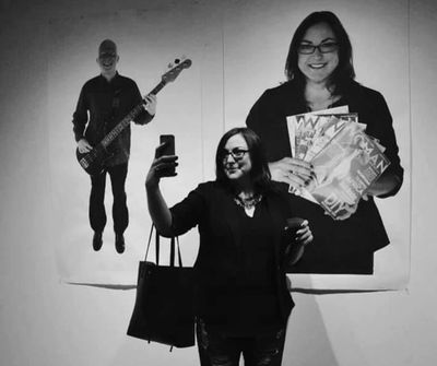 Woman taking selfie in front of large posters in black and white.