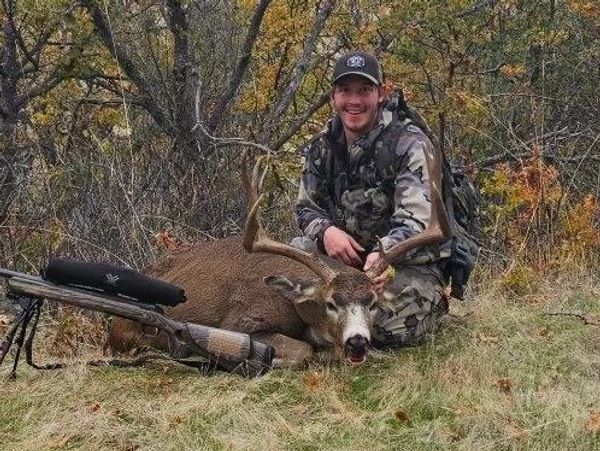 Hunter posing with a large deer and rifle in autumn forest.