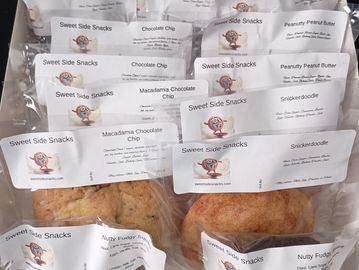 Assorted packaged baked goods labeled Sweet Side Snacks with flavors like Snickerdoodle and Macadamia Chocolate Chip.