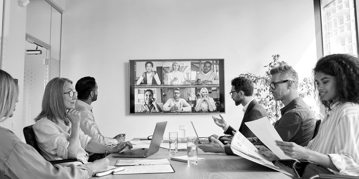 A hybrid meeting with in-person and remote participants engaged in discussion.