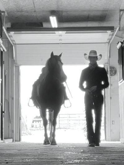 Silhouette of cowboy walking beside horse in barn.