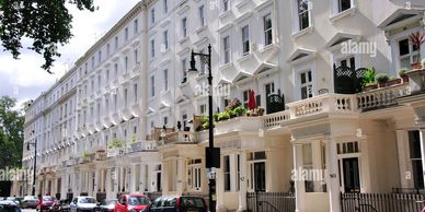 Row of elegant white Georgian-style townhouses with balconies and parked cars.