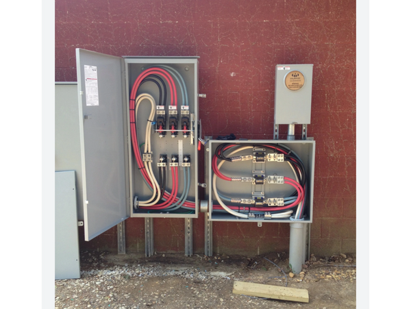 Open electrical panels with organized wiring against a red brick wall.