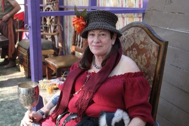 Woman in vintage dress and hat holding a goblet.