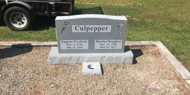 A gray granite headstone in a coping lot in a cemetery. 