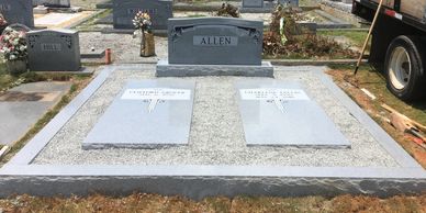 A gray granite headstone and 2 gray granite ledger markers inside of coping lot in a cemetery.