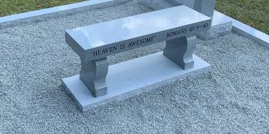 A gray granite bench inside a coping lot and beside a gray granite headstone. 
