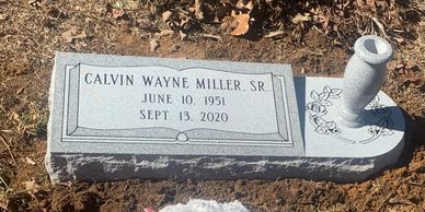A gray granite marker headstone with a gray turned granite vase in a cemetery.