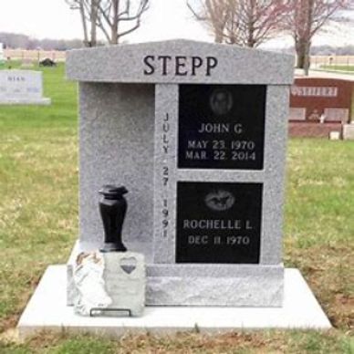 A two-crypt vertical mausoleum with a black granite turned vase in a cemetery.