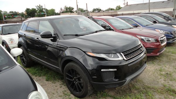 A black Range Rover Evoque parked among other cars on grass.