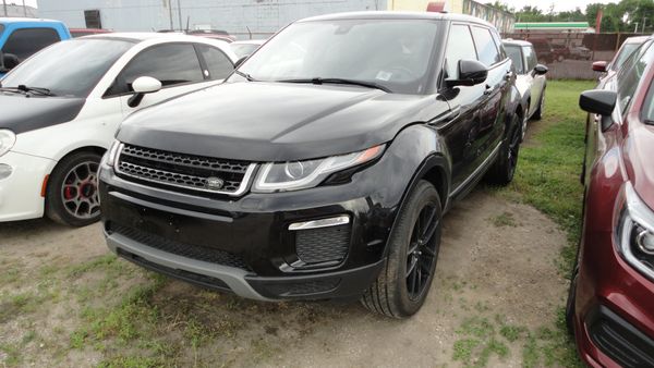 Black Land Rover SUV parked between other cars on a gravel lot.