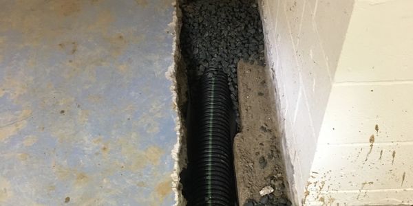 A drainage pipe installation in a trench along a wall with gravel bedding.