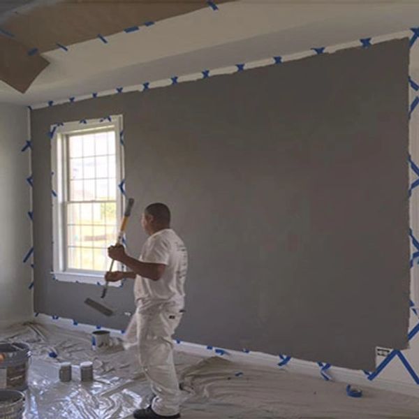 Painter applying gray paint to a wall with protective coverings.